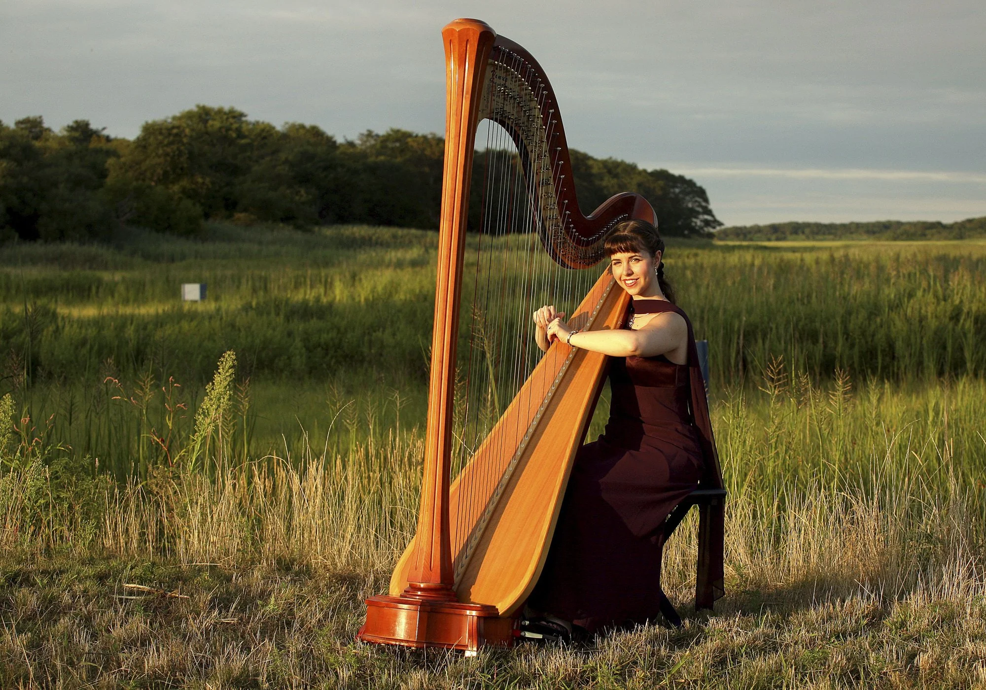 Harpist Katie Lynch is photographed at sunset with Quivet Creek Marsh behind her in Dennis, Massachusetts.