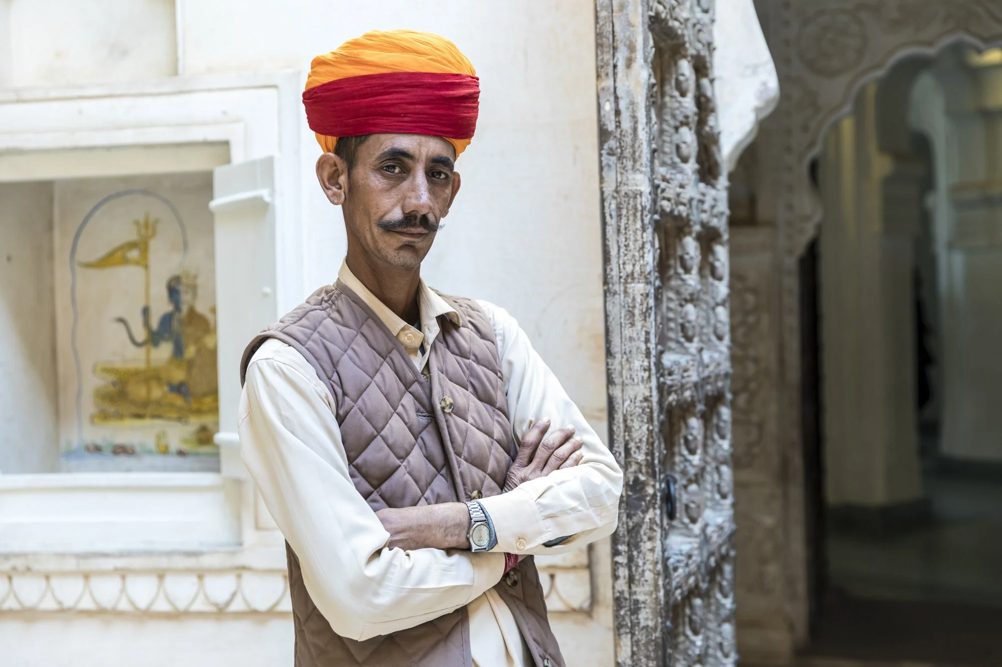 A palace guard in Rajasthan, his traditional pagri symbolizing honor and regional pride, stands for a portrait amid the historic stonework.