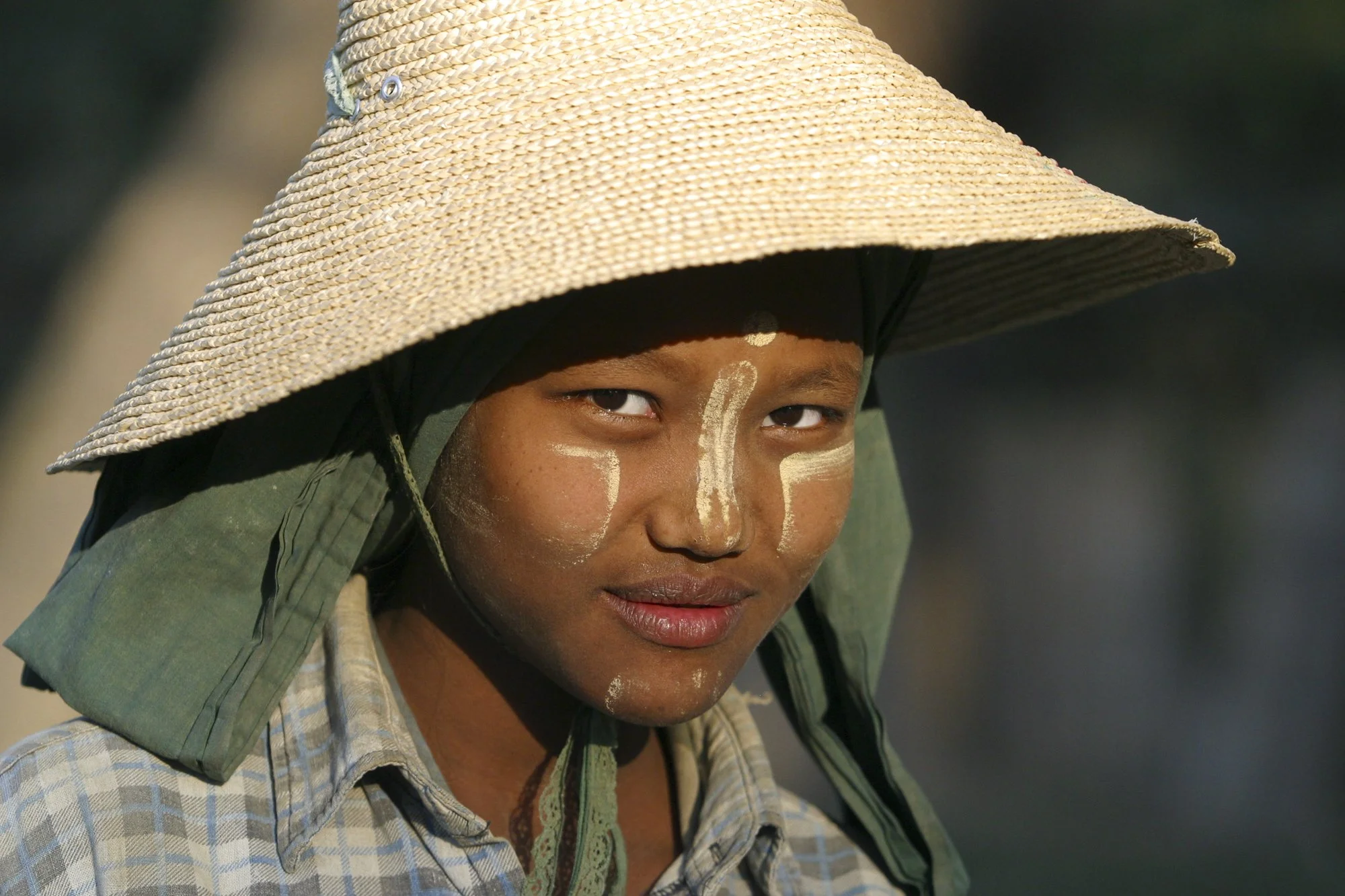 A young woman is photographed in Myanmar (Burma), her cheeks brushed with thanaka—a natural paste made from ground tree bark that has been used for centuries as sun protection, skincare, and decoration.