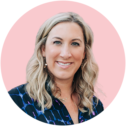 Headshot of a woman with blonde hair smiling, wearing earrings and a dark patterned top against a pink background.