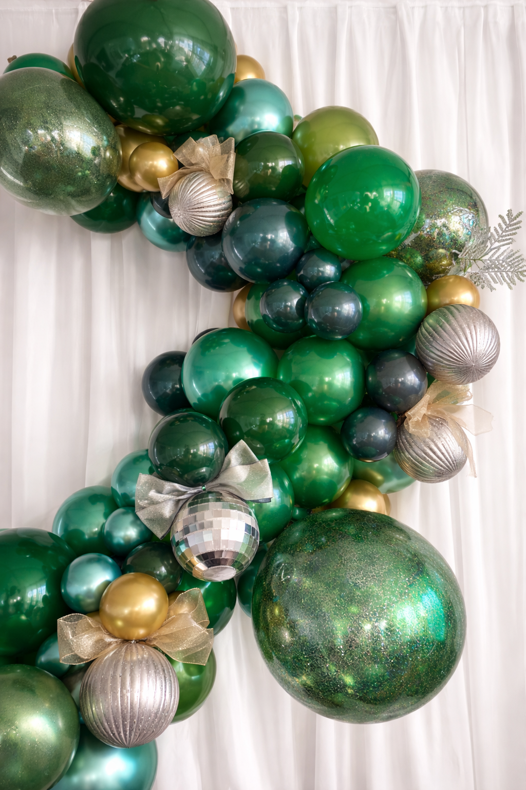 Rich emerald green and gold organic balloon arch with oversized statement balloons.
