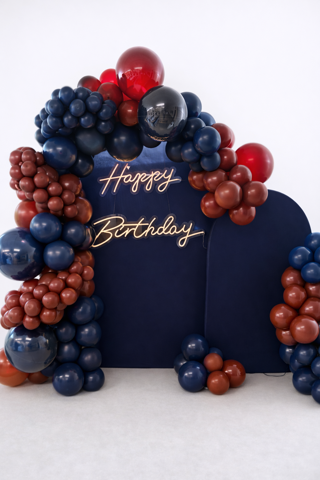 Modern navy, burgundy and copper balloon arch with illuminated “Happy Birthday” sign.