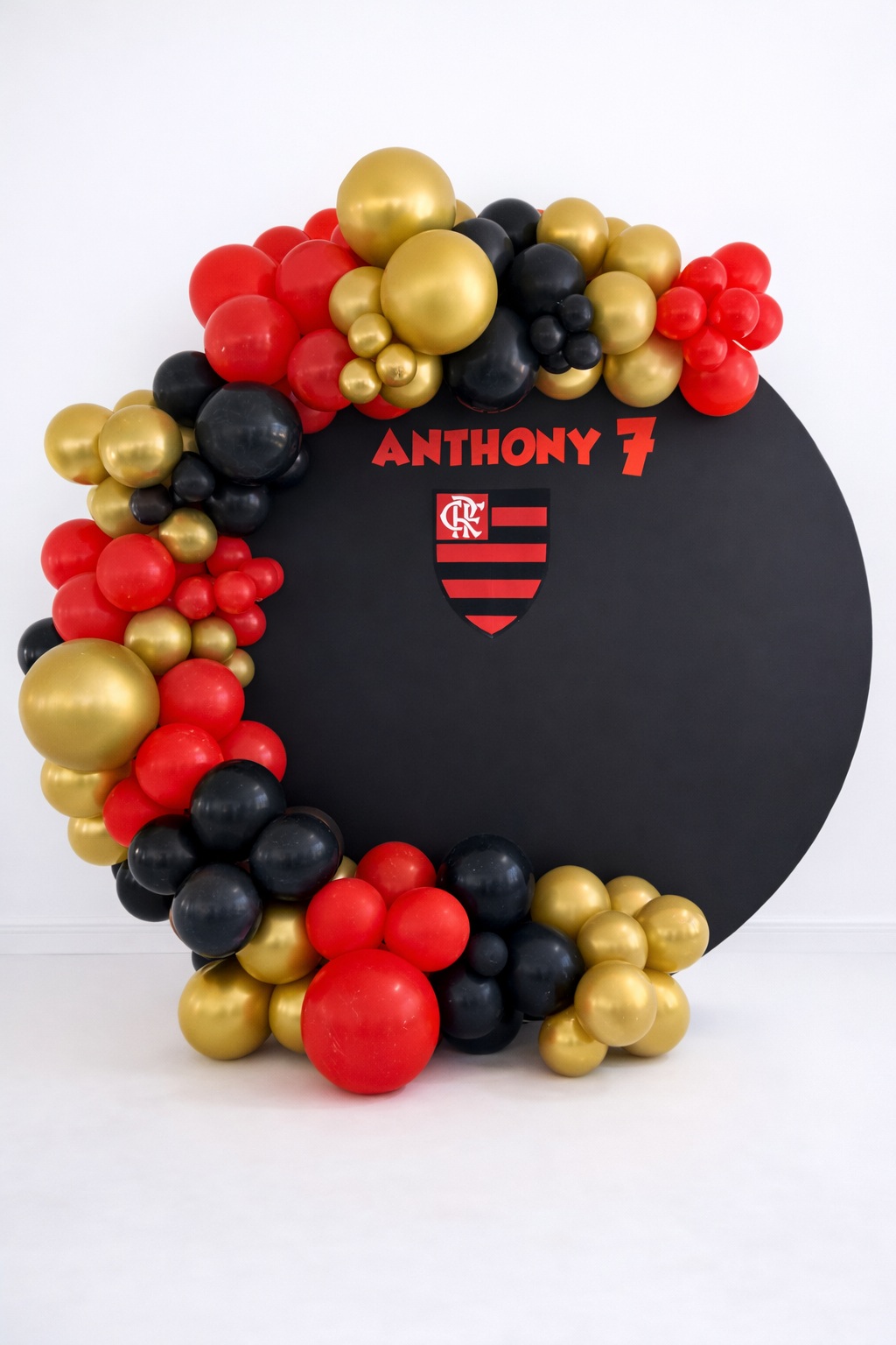 Modern black round backdrop featuring a red, black and gold organic balloon arrangement with custom name and sports-inspired details.