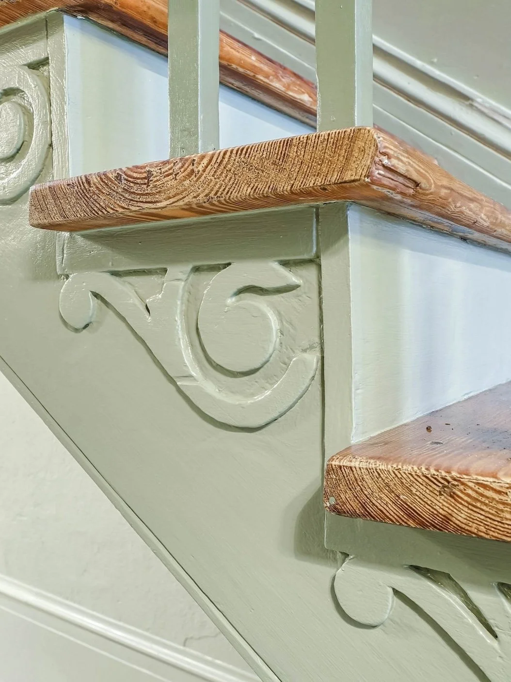 Close-up of decorative wooden corbels and flooring on a staircase, with detailed carved designs and painted in a light green color.