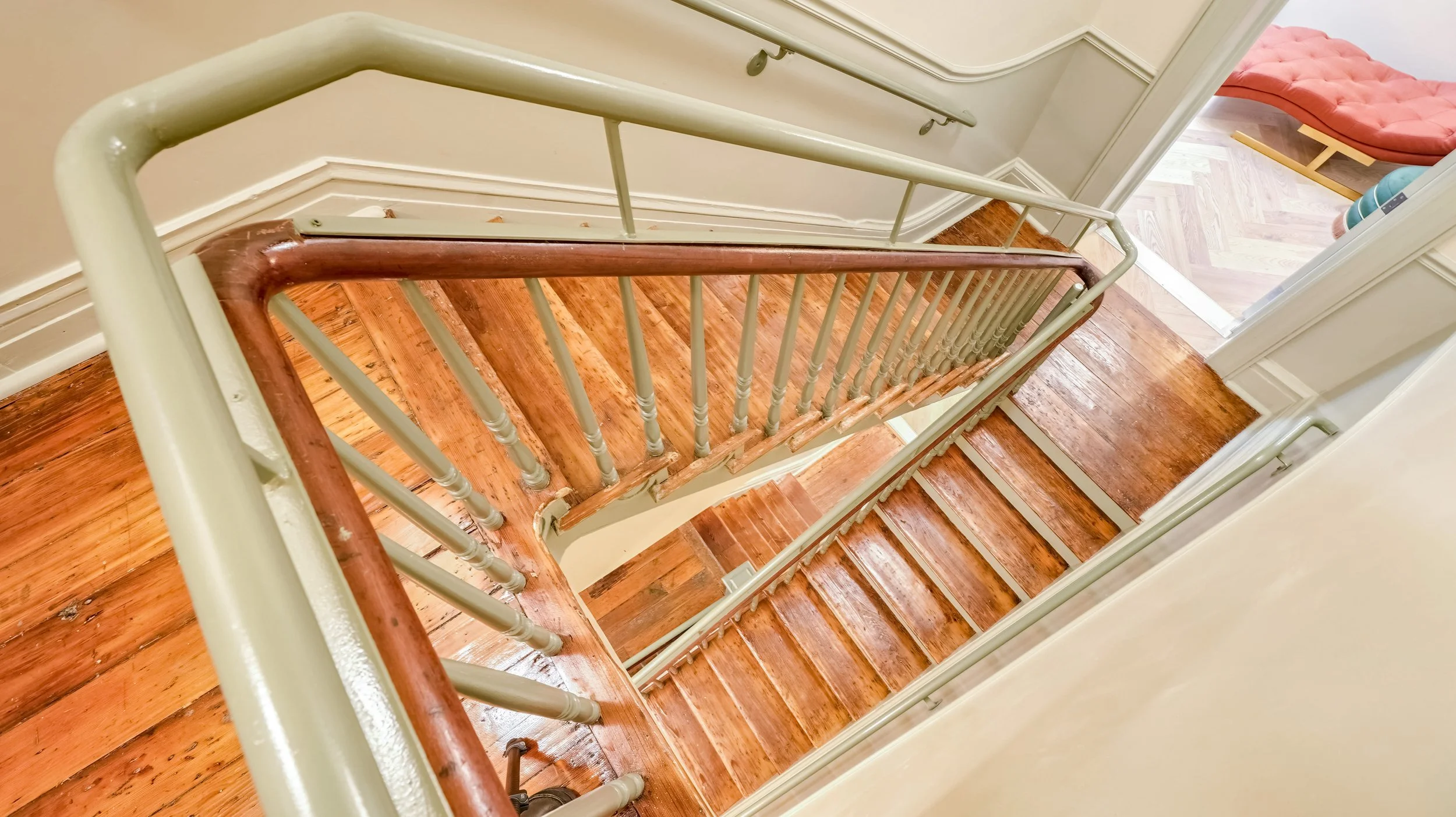 Top-down view of a wooden staircase with beige painted railings and a polished wood handrail.