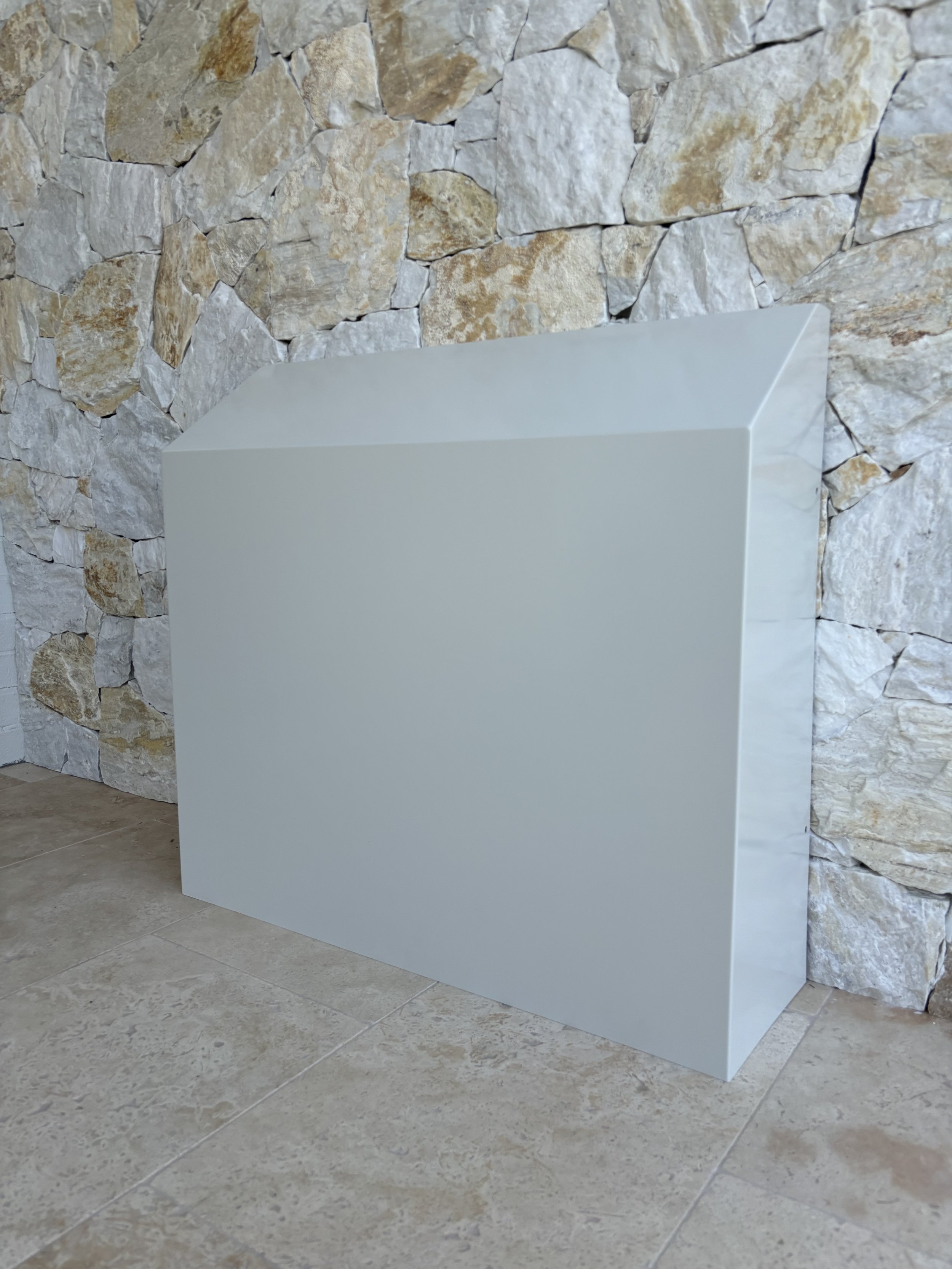 A plain white rectangular box with a slanted top against a stone wall background.