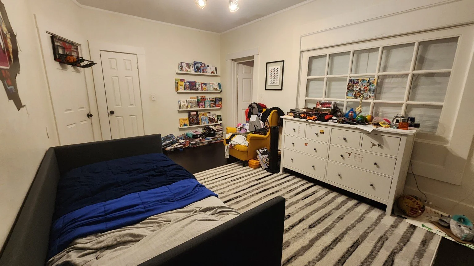 Boy’s bedroom before the refresh with a black bed, white dresser, book ledges and limited floor space