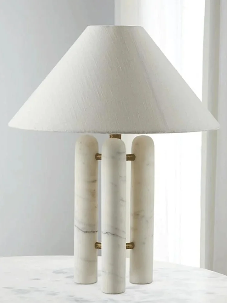Table lamp with three vertical white marble columns connected by brass supports, finished with a tapered natural fabric shade; perfect for a console, sideboard, or bedside table.