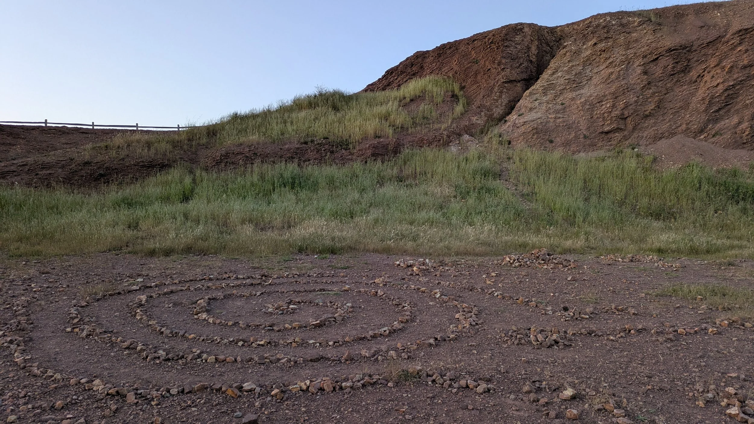 Spiral labryinth on Bernal Hill, San Francisco. Made of rocks at the edge of a patch of grass. Blue sky at dusk in the background. Copyright Shasta Garcia