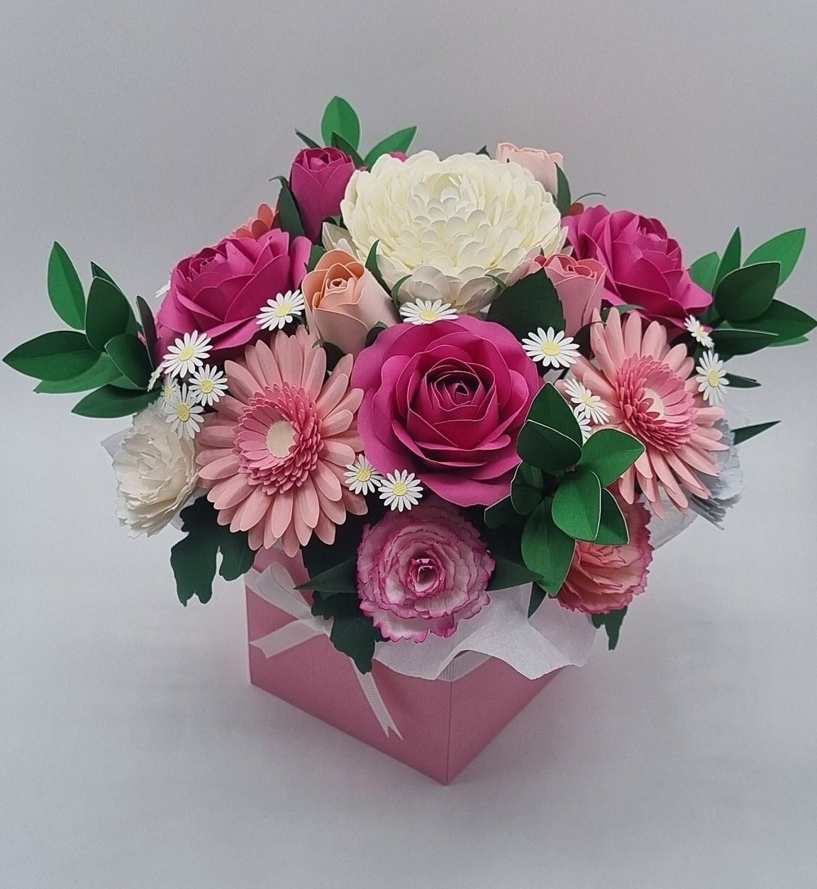 A paper-crafted floral arrangement with pink, white, and peach paper flowers in a pink box.