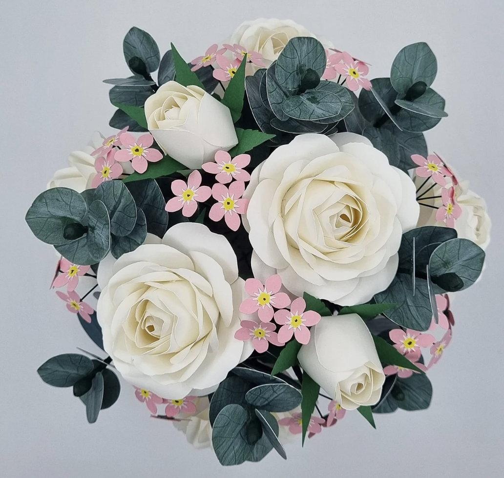 A bouquet of artificial flowers including white roses, pink small flowers, green leaves, and eucalyptus with a plain light gray background.