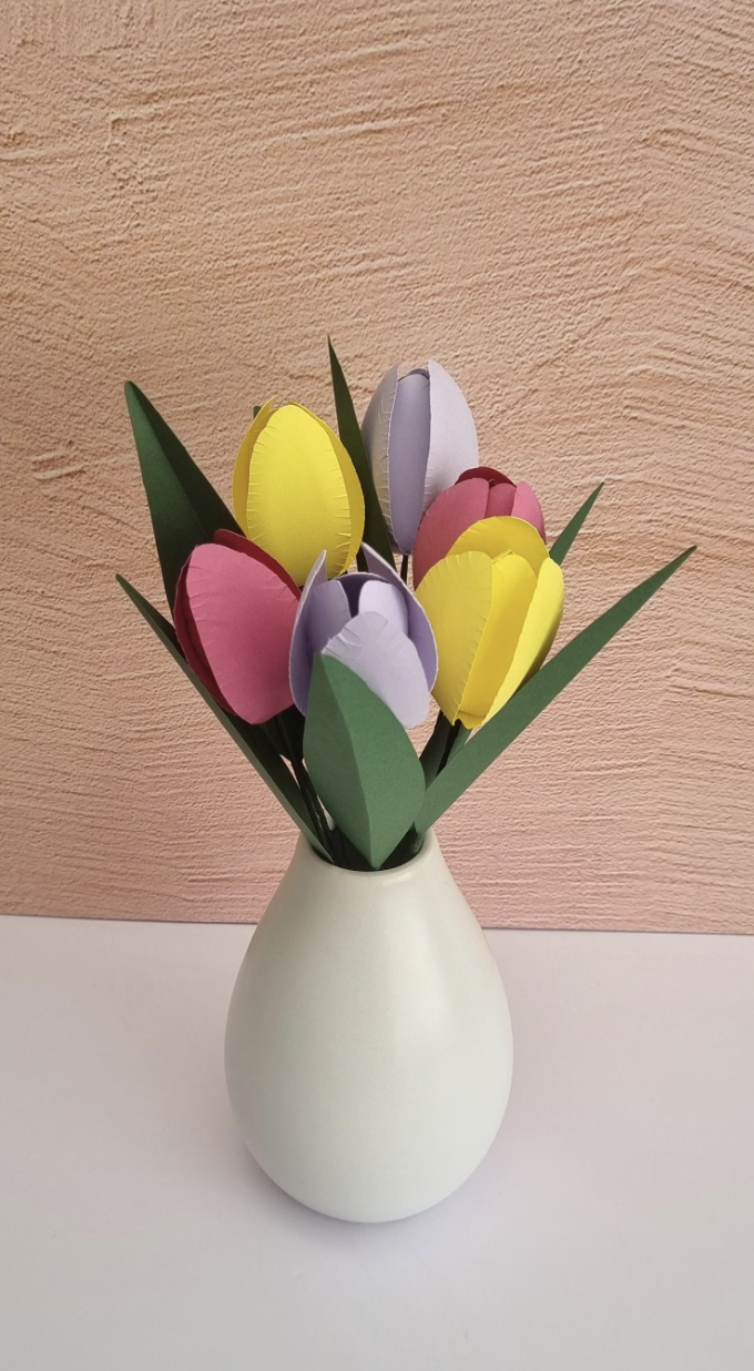Paper craft tulip bouquet in a cream vase against a peach textured background.