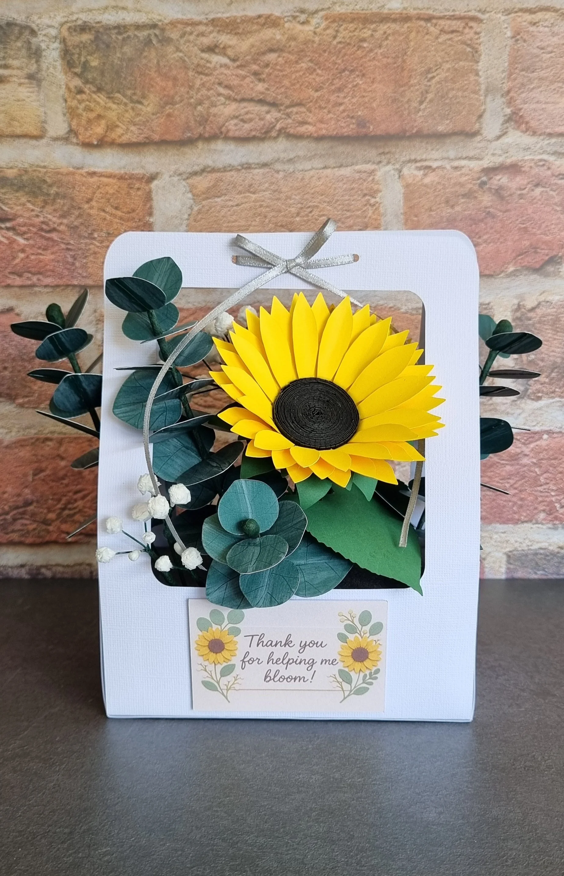 Front view of a handmade sunflower paper flower arrangement in a white gift box with eucalyptus, baby’s breath, and a “Thank you for helping me bloom!” plaque..jpg