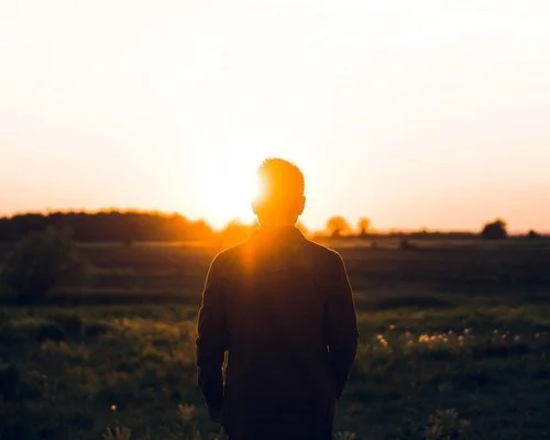 Silhouette of a person standing outdoors during sunset with sun behind them, in a rural landscape