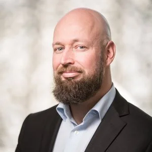 Portrait of a man with a beard wearing a suit and light blue shirt, smiling at the camera.