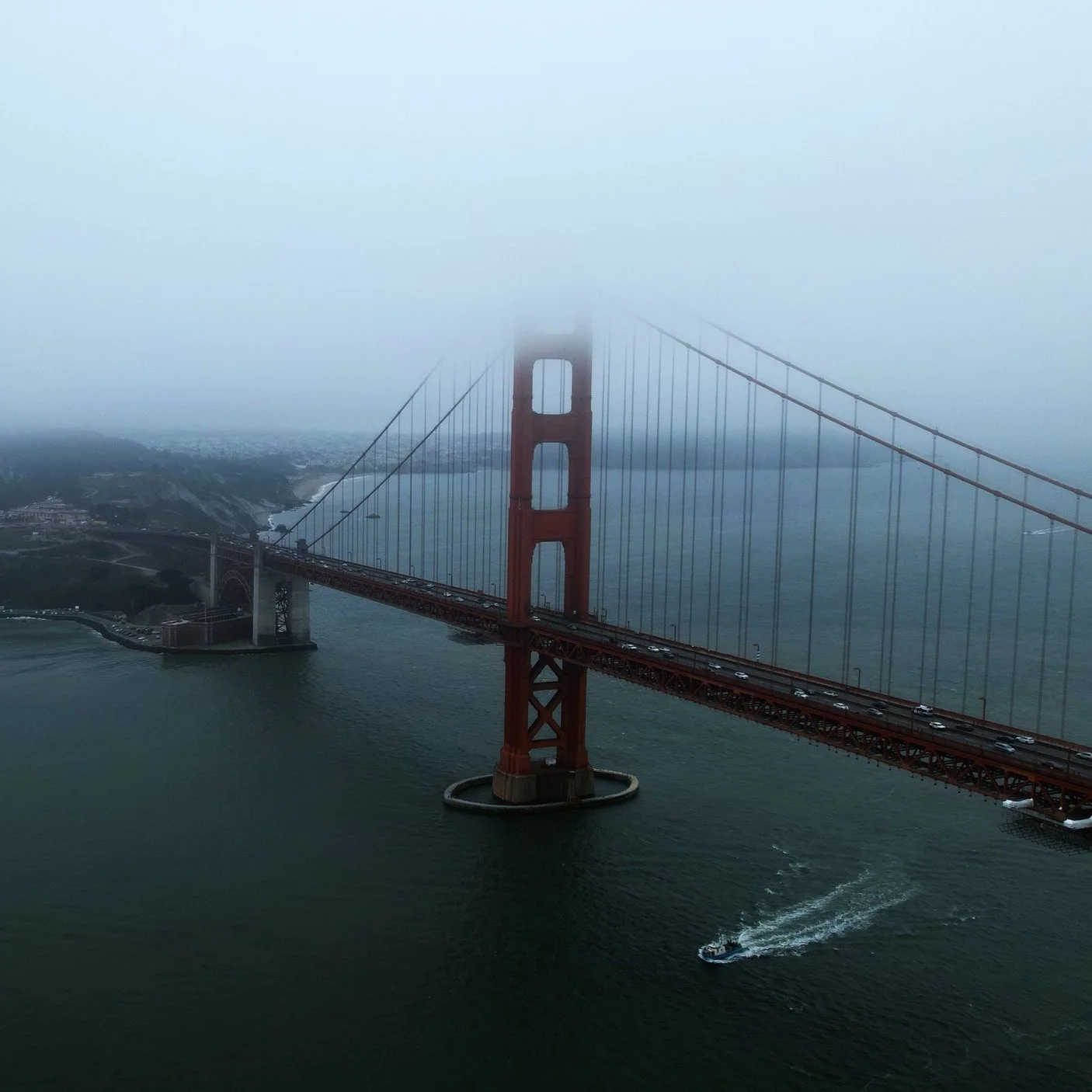 The Golden Gate Bridge partially shrouded in fog, spanning across the water with cars on the bridge and a boat moving underneath.