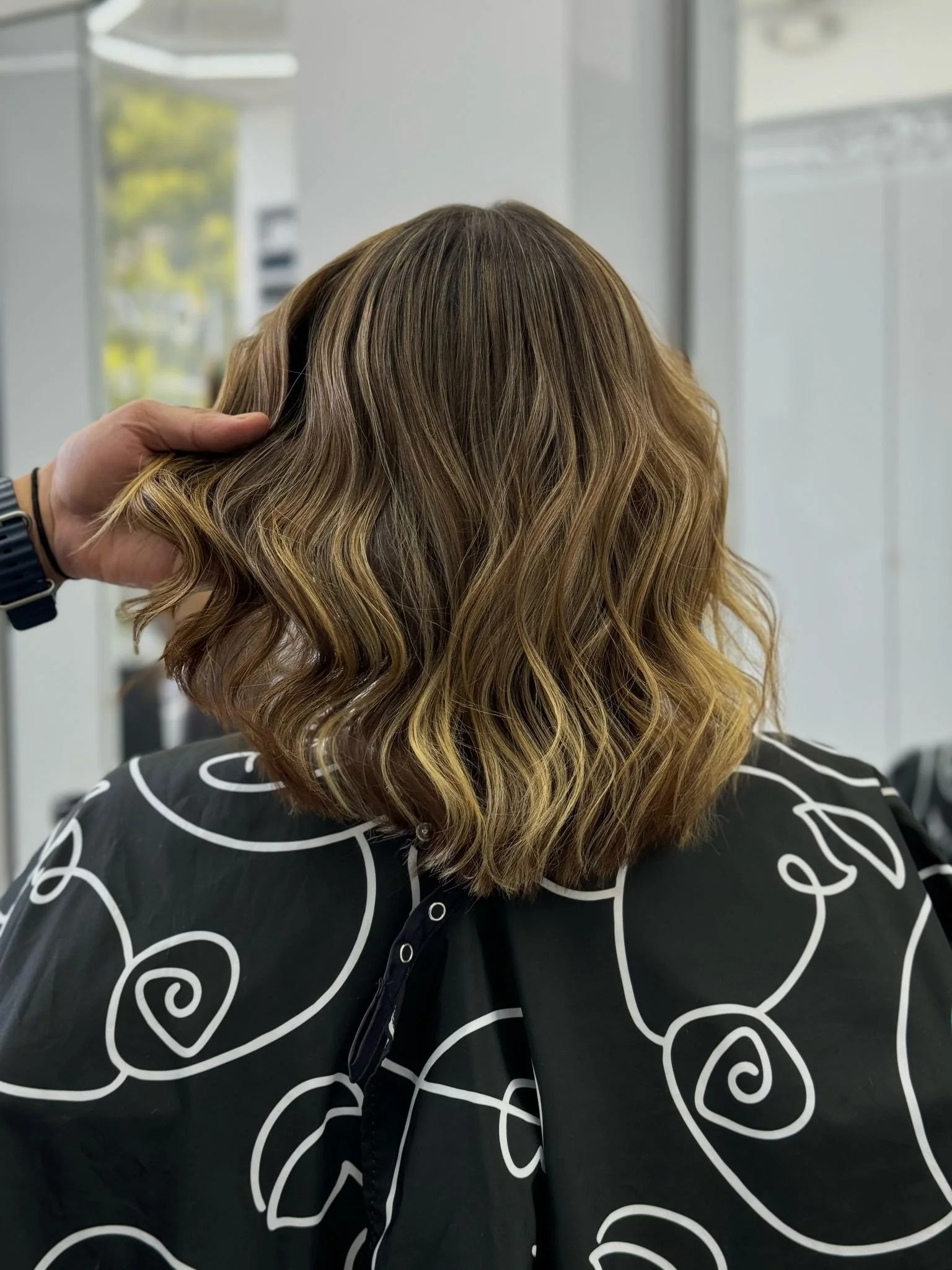 Back of a woman's head with styled, wavy hair in shades of blonde and light brown, in a salon setting.