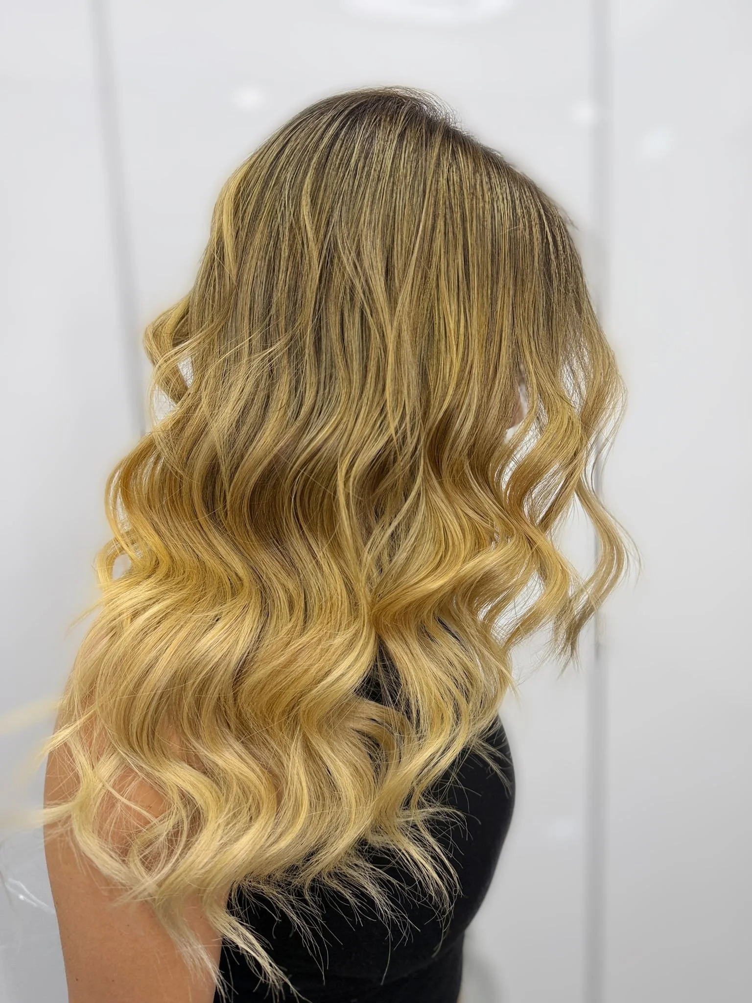 Wavy blonde hair with darker roots, styled in loose curls on a person in a black top.
