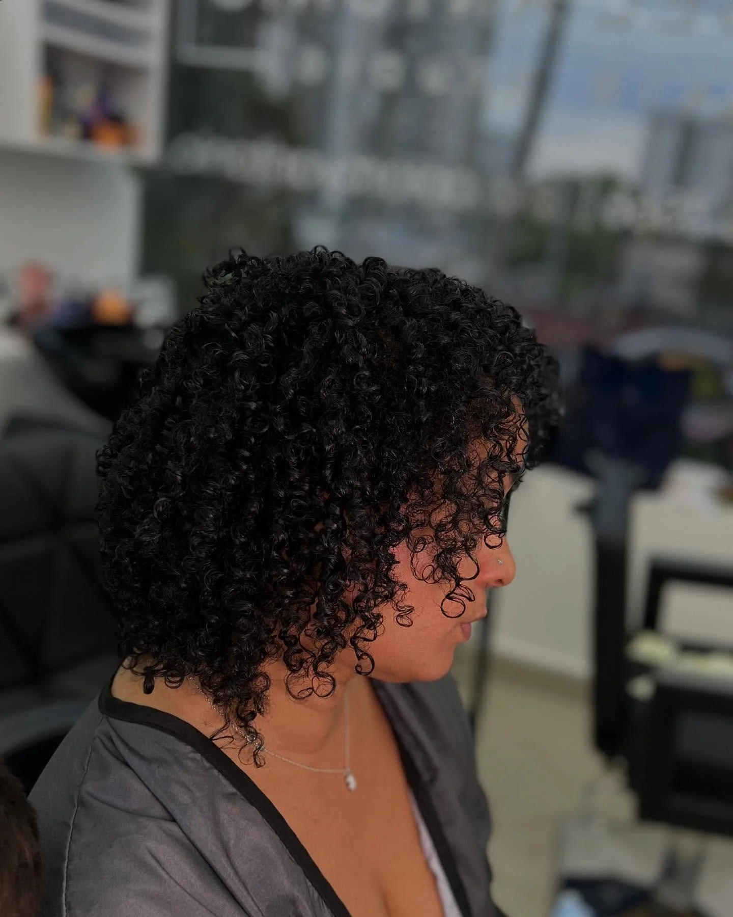 Side view of a woman with dark, curly hair in a salon environment.