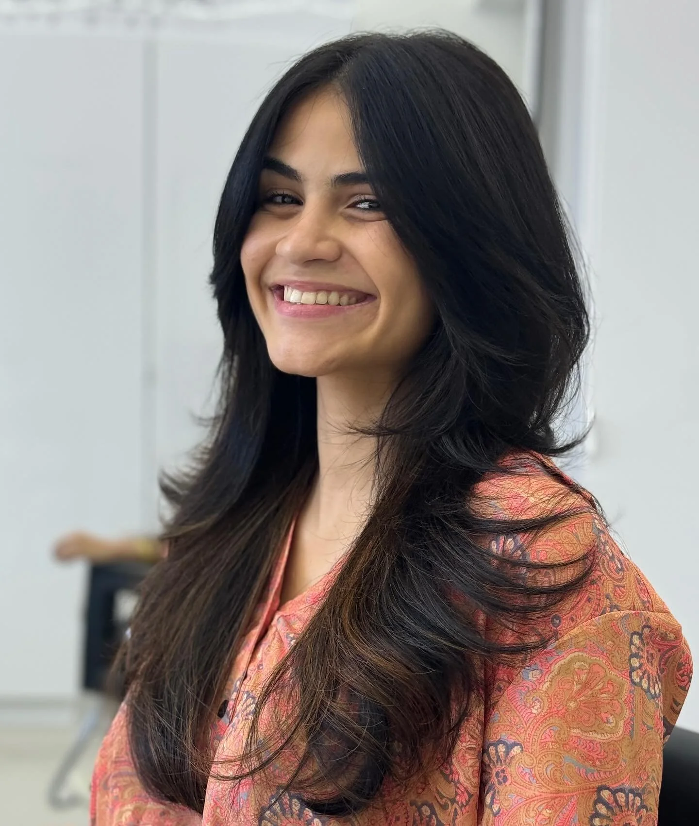 A woman with long black hair smiling in an indoor setting.