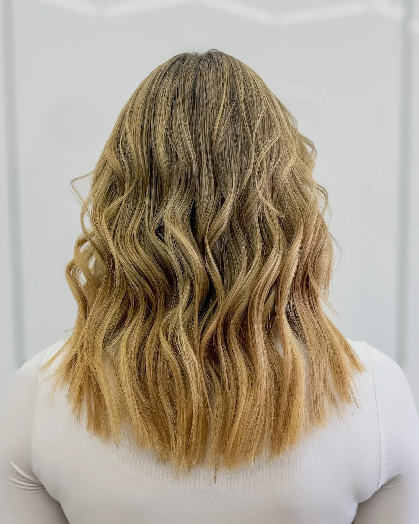 Back of a person with blonde, wavy hair wearing a white shirt.
