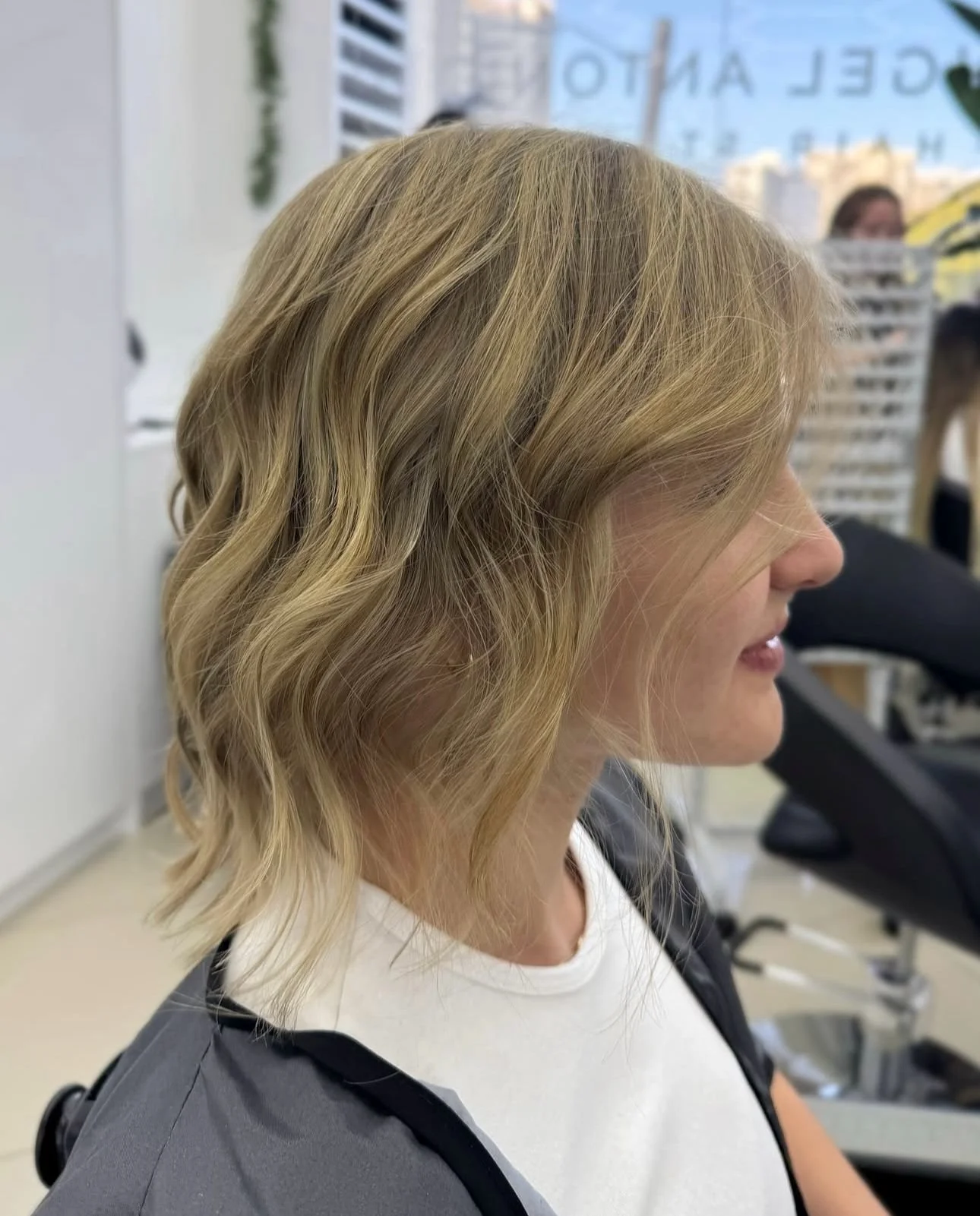 A woman with blonde, wavy shoulder-length hair sitting in a salon chair.