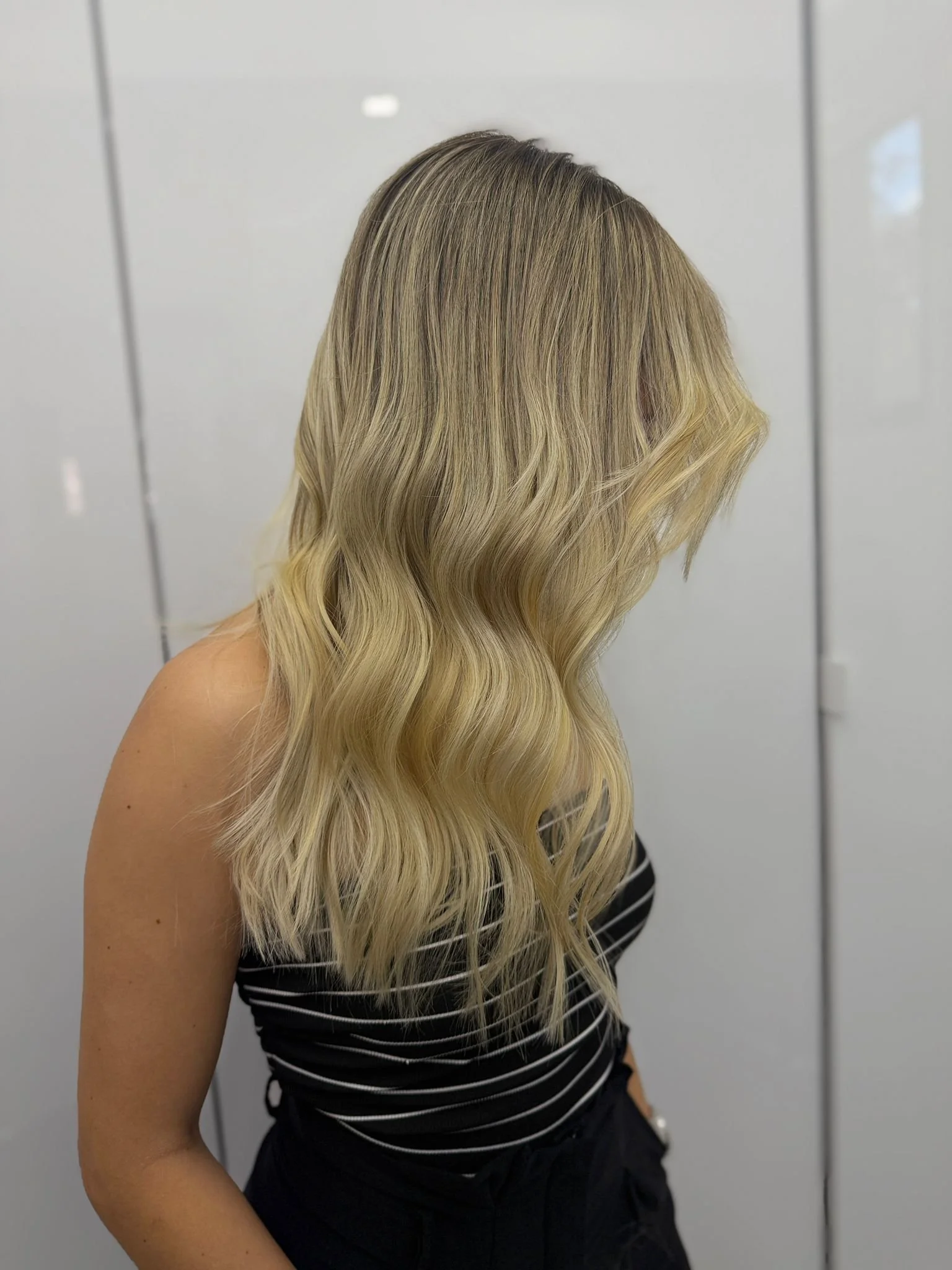 A woman with long, wavy blonde hair, turned slightly away from the camera, wearing a black and white striped top.