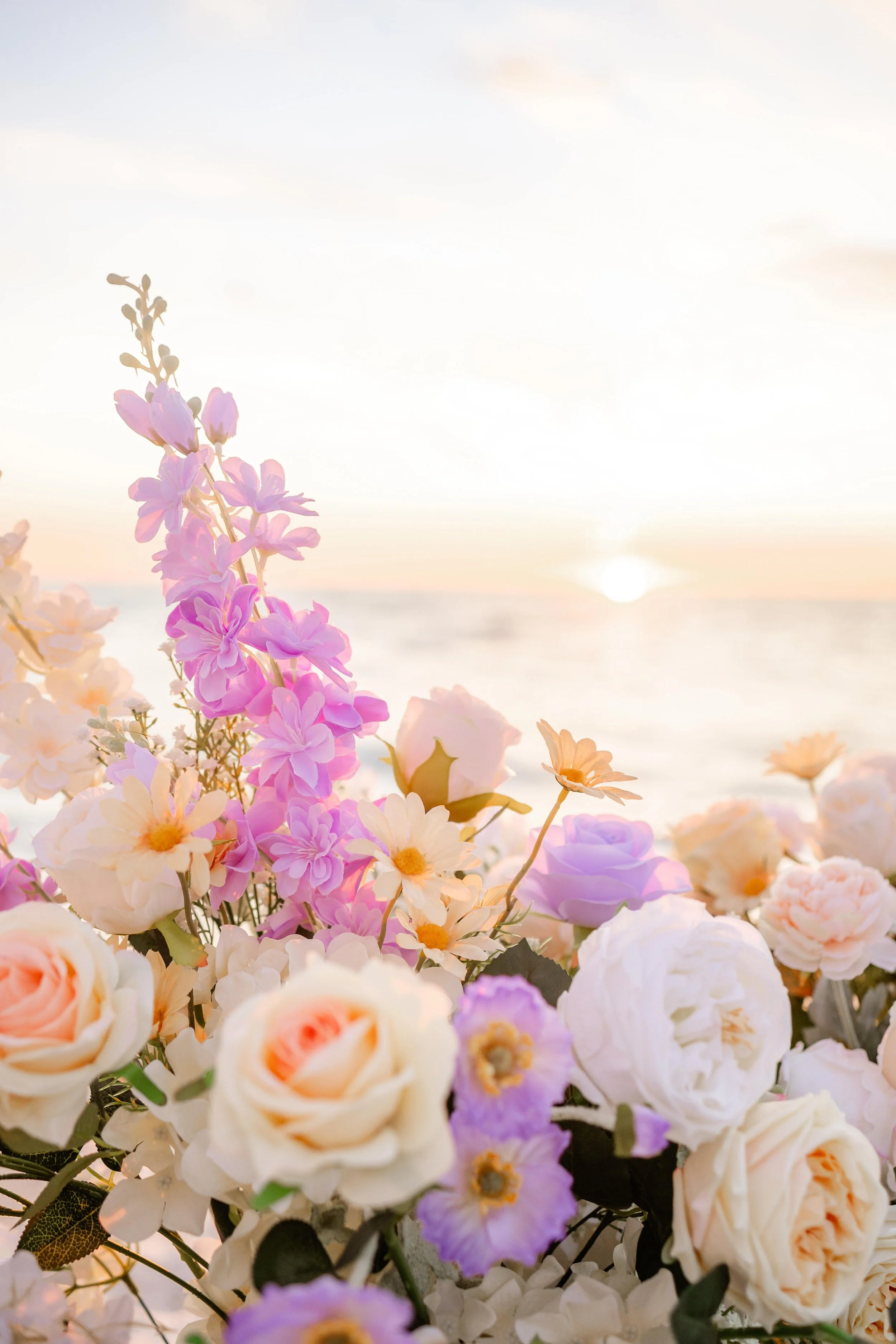 Arrangement of pink, white, and purple flowers near a body of water with the sun setting in the background at the beach in Panama City beach.