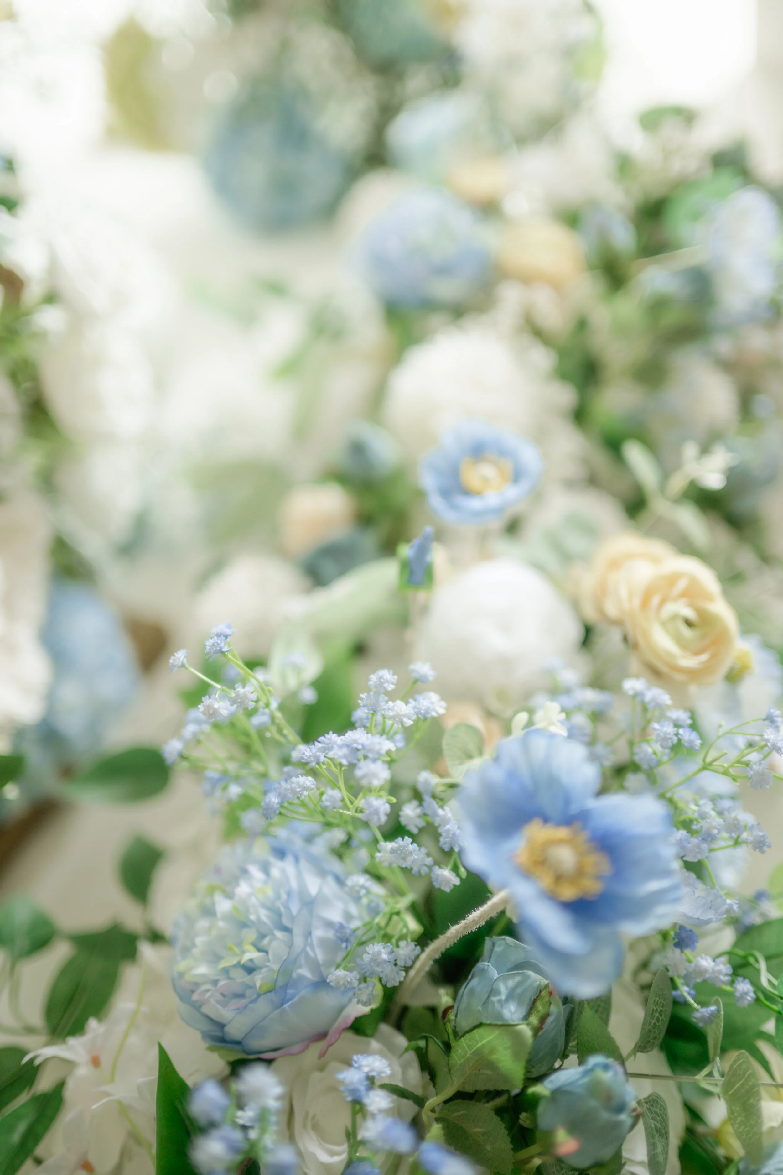 Close-up of pastel-colored flowers, including blue, white, and cream roses, with green leaves surrounding them for floral rentals for weddings in the panhandle.