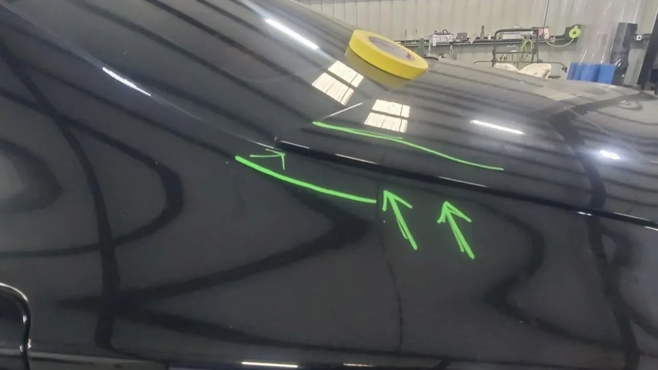 Car with green arrows drawn on the rear roof panel and a yellow tape roll on top, indicating repair or inspection.