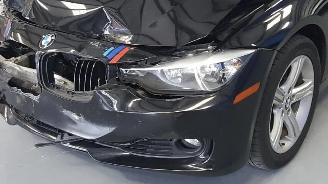 Damaged front end of a black BMW car with a dented bumper and broken grille.