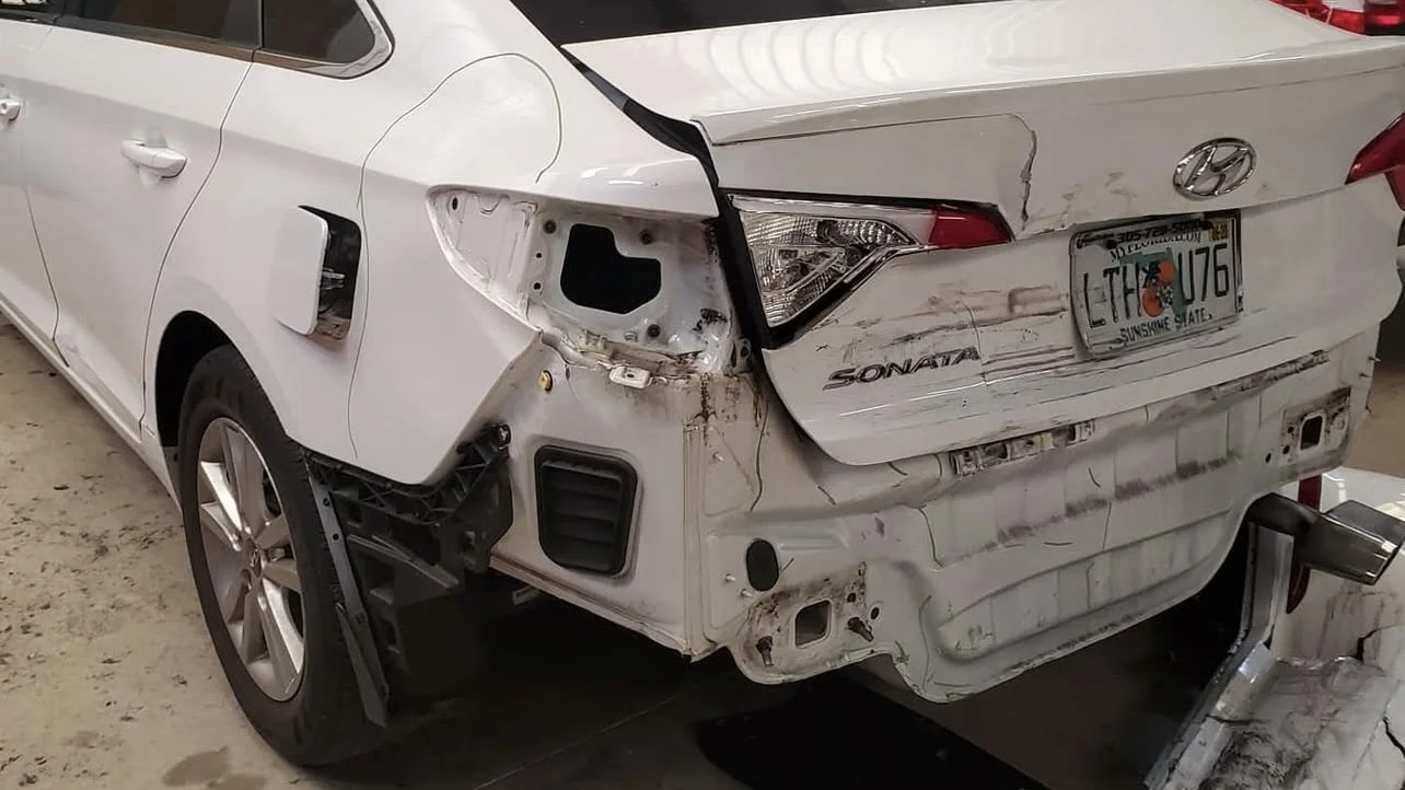Damaged rear of a white Hyundai Sonata with a Florida license plate, showing missing rear bumper and broken taillight.