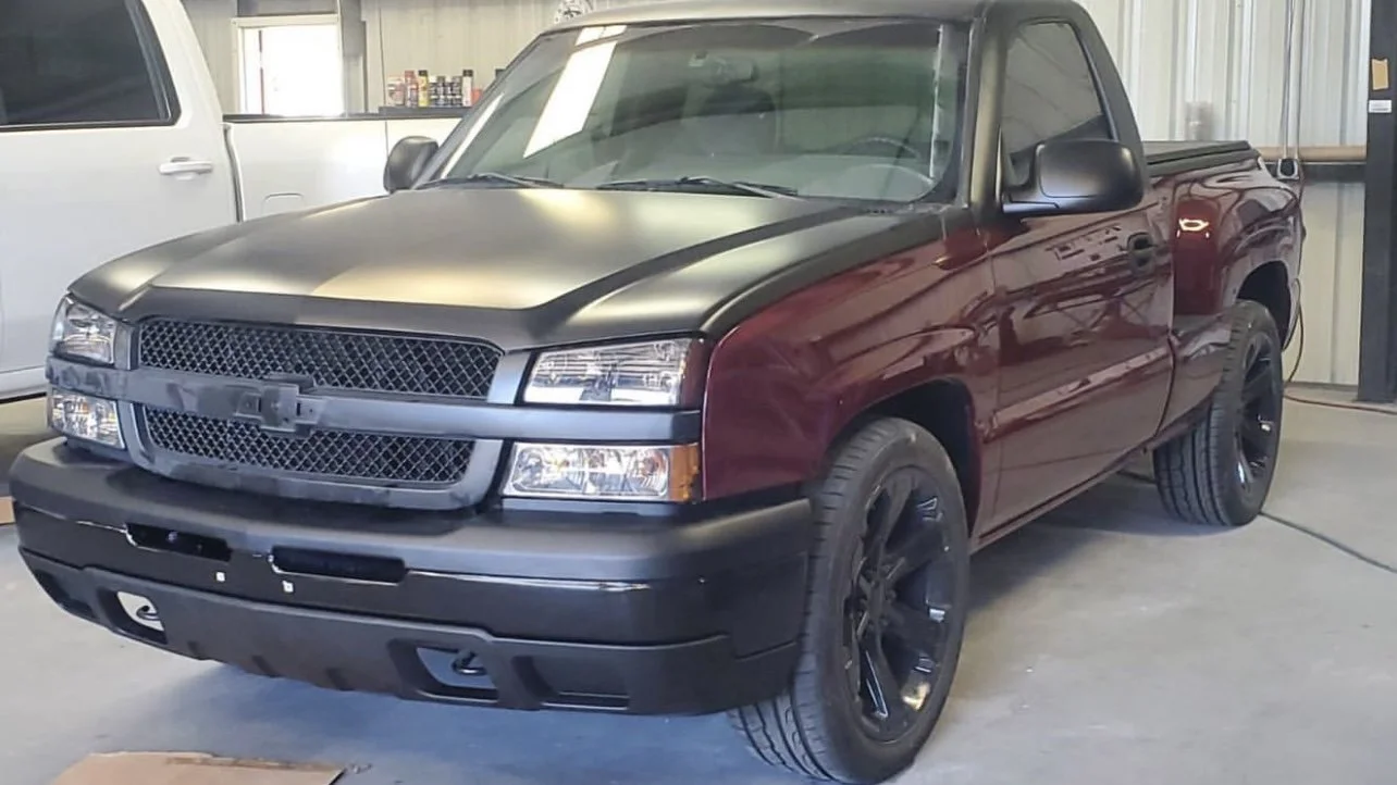 Custom Chevrolet pickup truck with a matte black hood and rims, maroon body, parked in a garage.