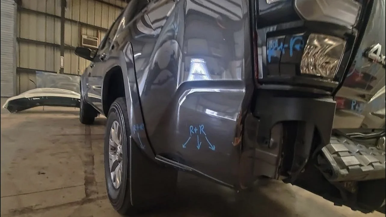 Close-up of a damaged truck rear corner with markings in a garage, indicating repair areas.