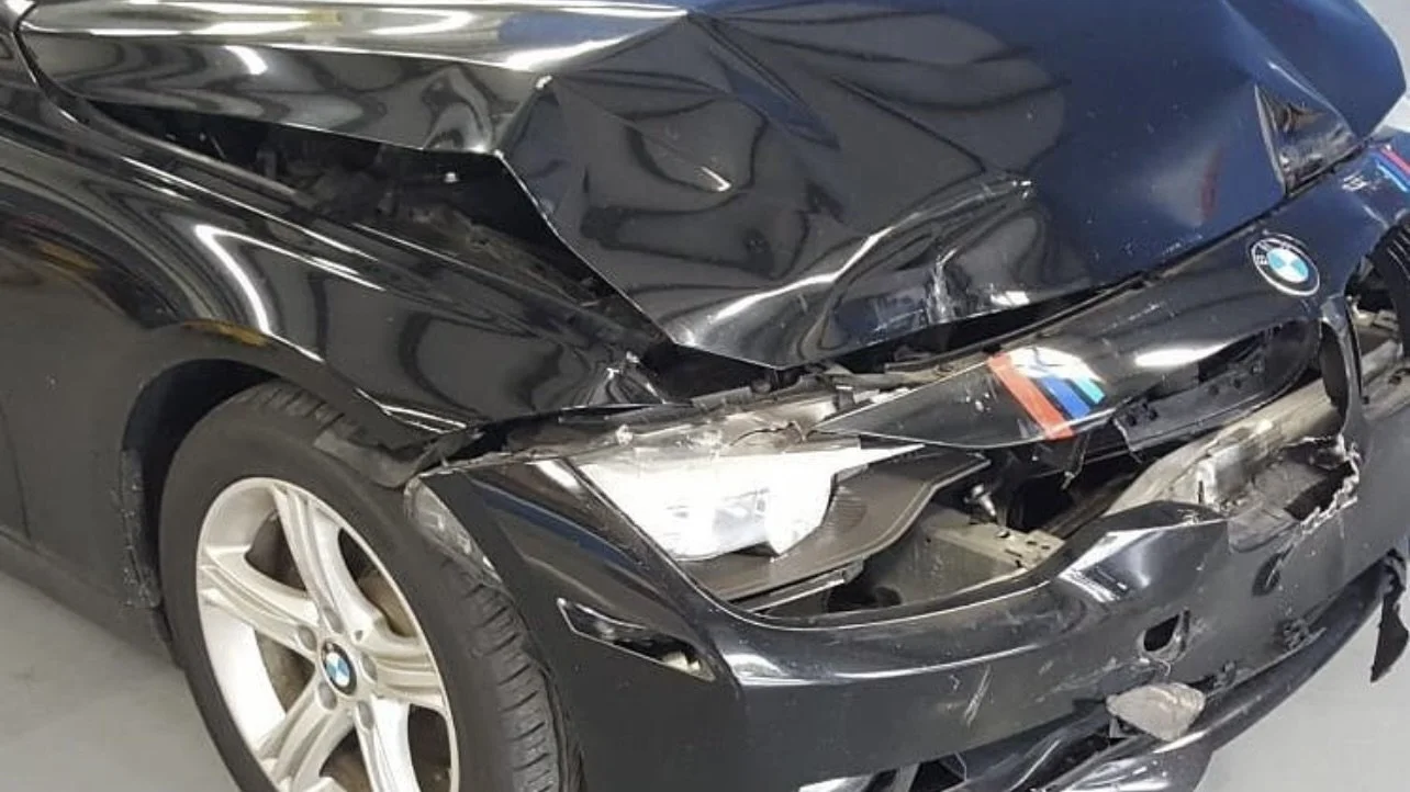 Damaged black BMW car with front-end collision damage, including a crumpled hood and broken headlight.