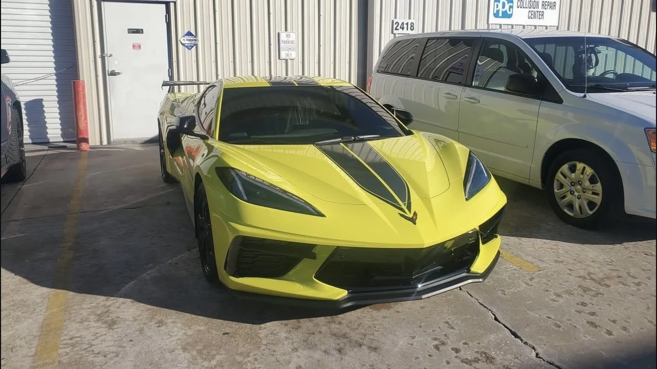 Yellow sports car with black stripes parked next to a white van by a garage.