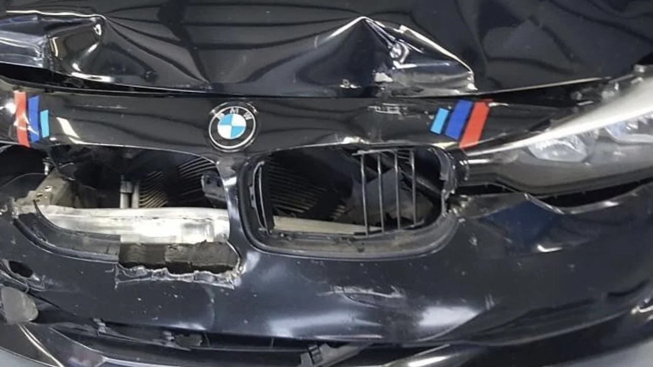 Front view of a damaged black BMW car with a dented hood and broken grille.