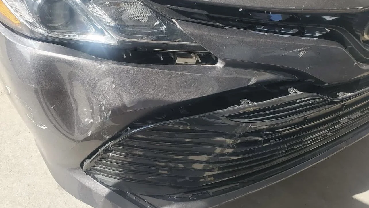 Close-up of a gray car with front bumper damage and scratches.