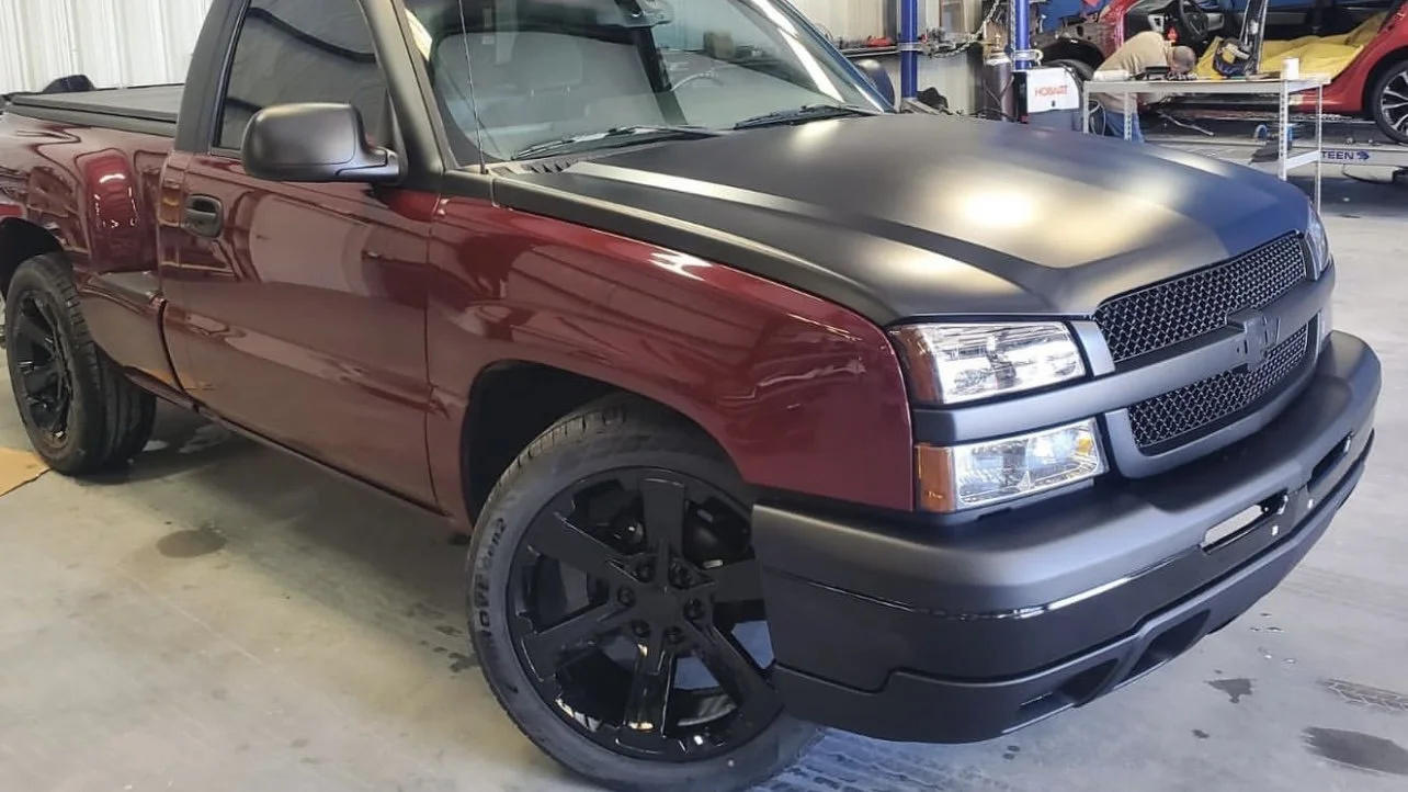 Customized pickup truck with a matte black hood and maroon body, featuring black rims, parked indoors.