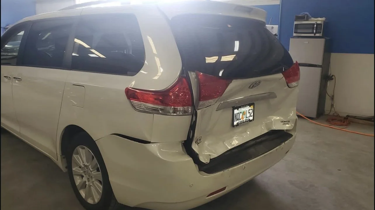 White SUV with rear end damage parked indoors.