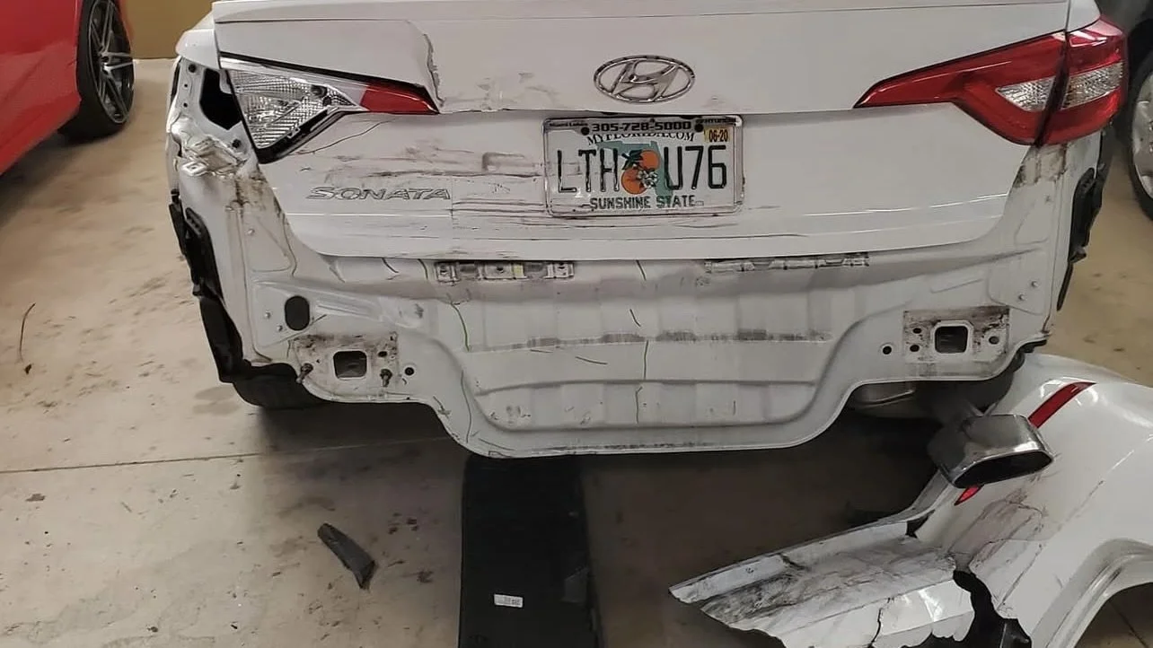 Damaged rear of a white Hyundai Sonata with a Florida license plate in a garage setting.