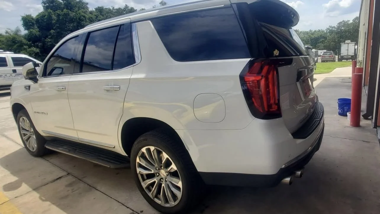 White SUV parked on a driveway near a garage, with open rear hatch.