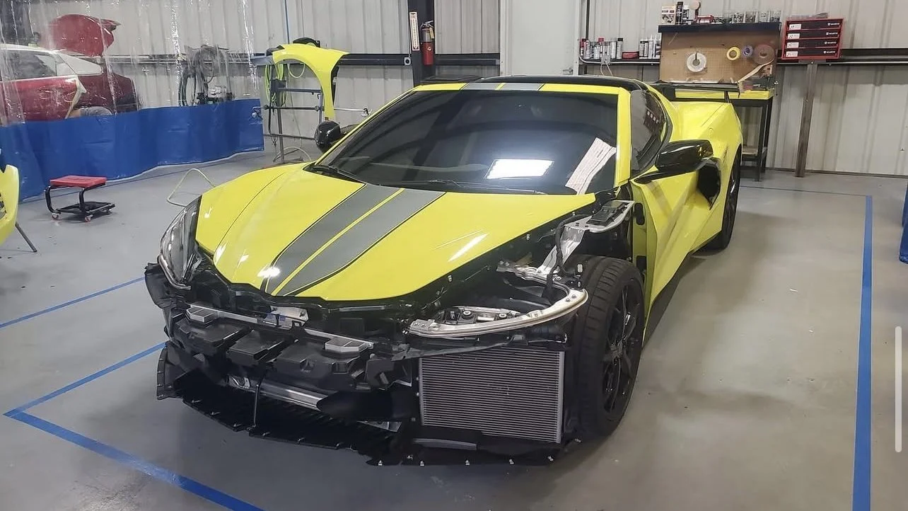 Yellow sports car with front bumper removed, inside a workshop with repair equipment.