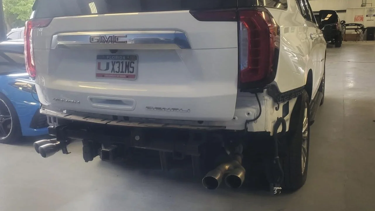 White GMC Denali SUV with partially removed rear bumper in a garage, Florida license plate visible.
