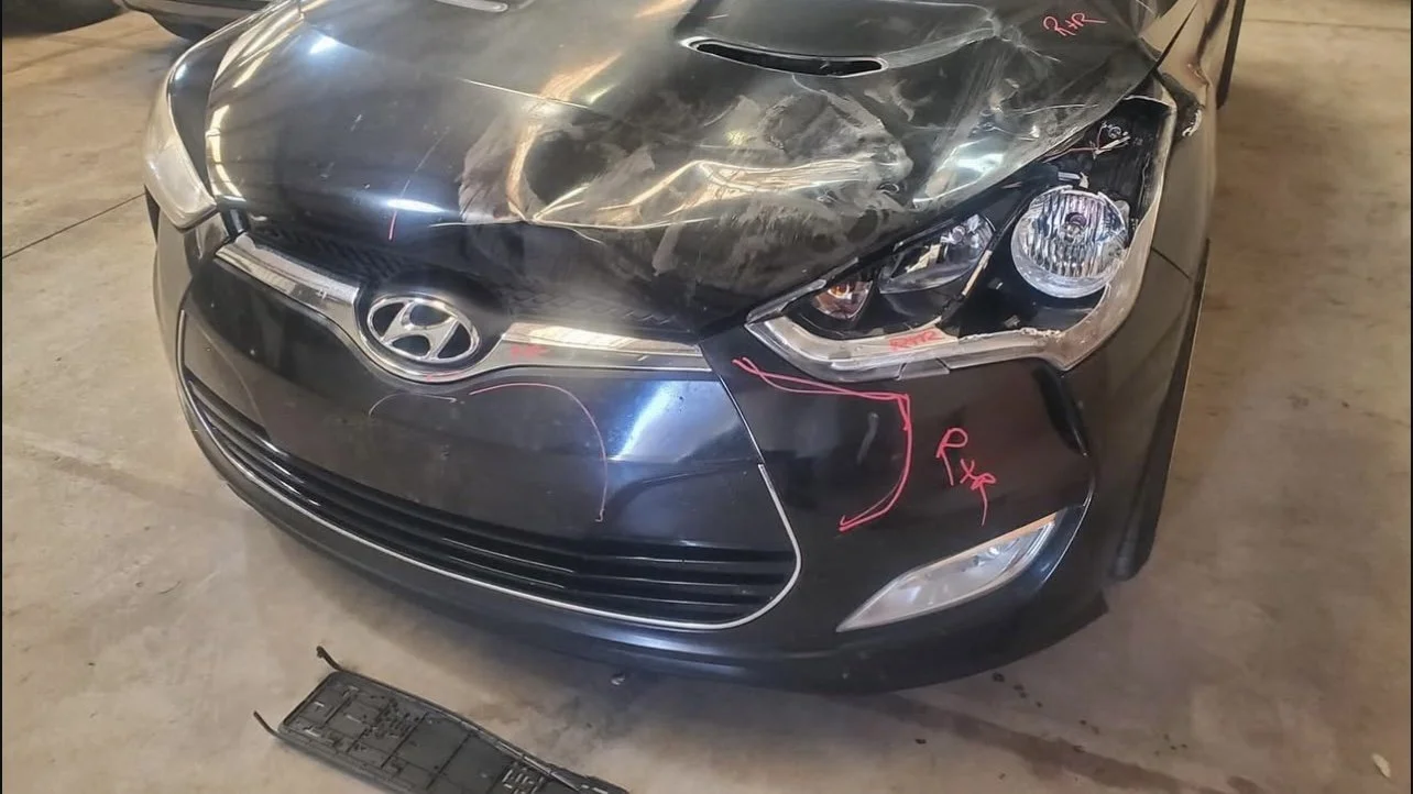 Front view of a damaged black Hyundai car with significant damage to the hood and front bumper.