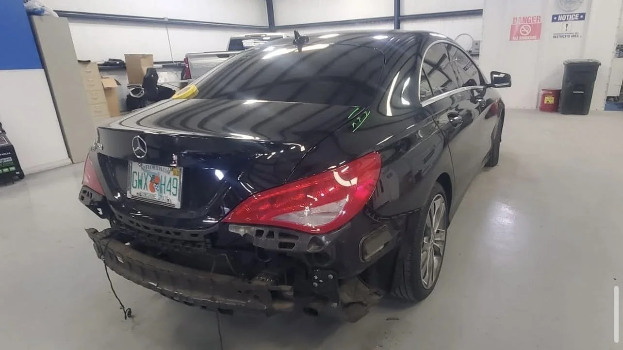 Black Mercedes car with rear bumper missing, parked in a garage.