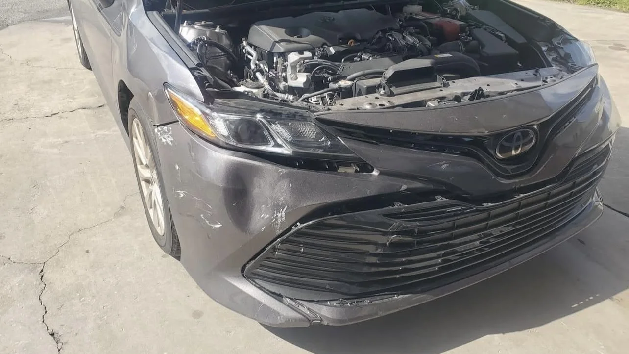 Damaged front of a gray car with hood open, showing the engine and visible scratches on the bumper.