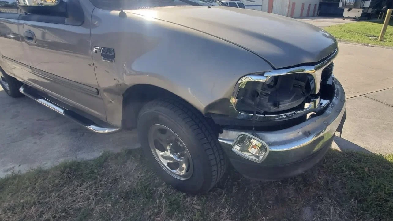 Damaged gray pickup truck with front-end headlight damage on a concrete driveway.
