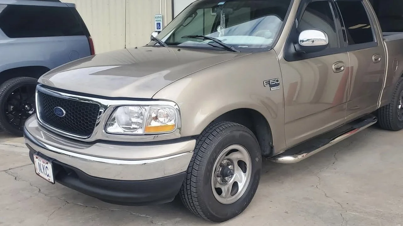 Beige Ford F-150 pickup truck parked beside a building, with another vehicle partially visible in the background.