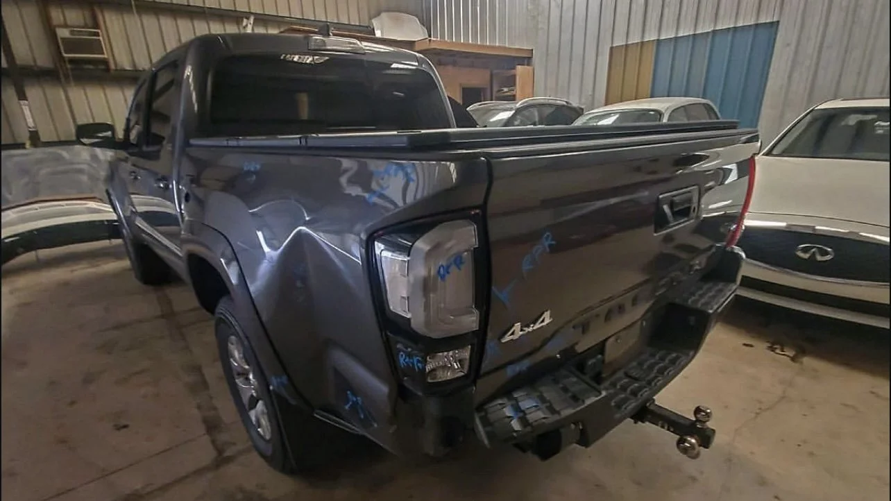 Dark gray pickup truck with rear-end damage parked in a garage, surrounded by other cars.
